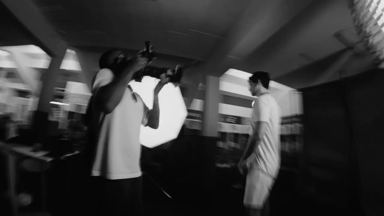Black and white handheld frame of a crew filming inside a newsroom.