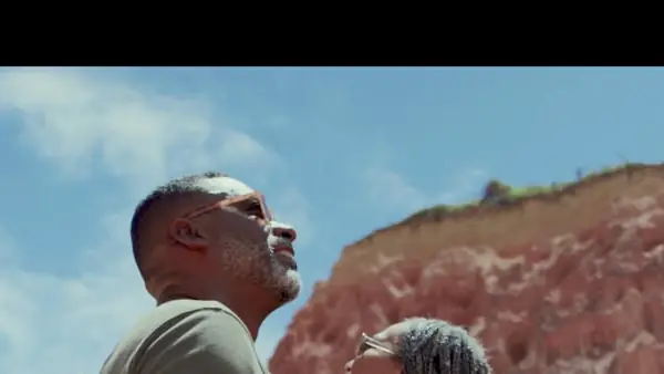 A couple looking up at red sandstone cliffs under a bright sky.