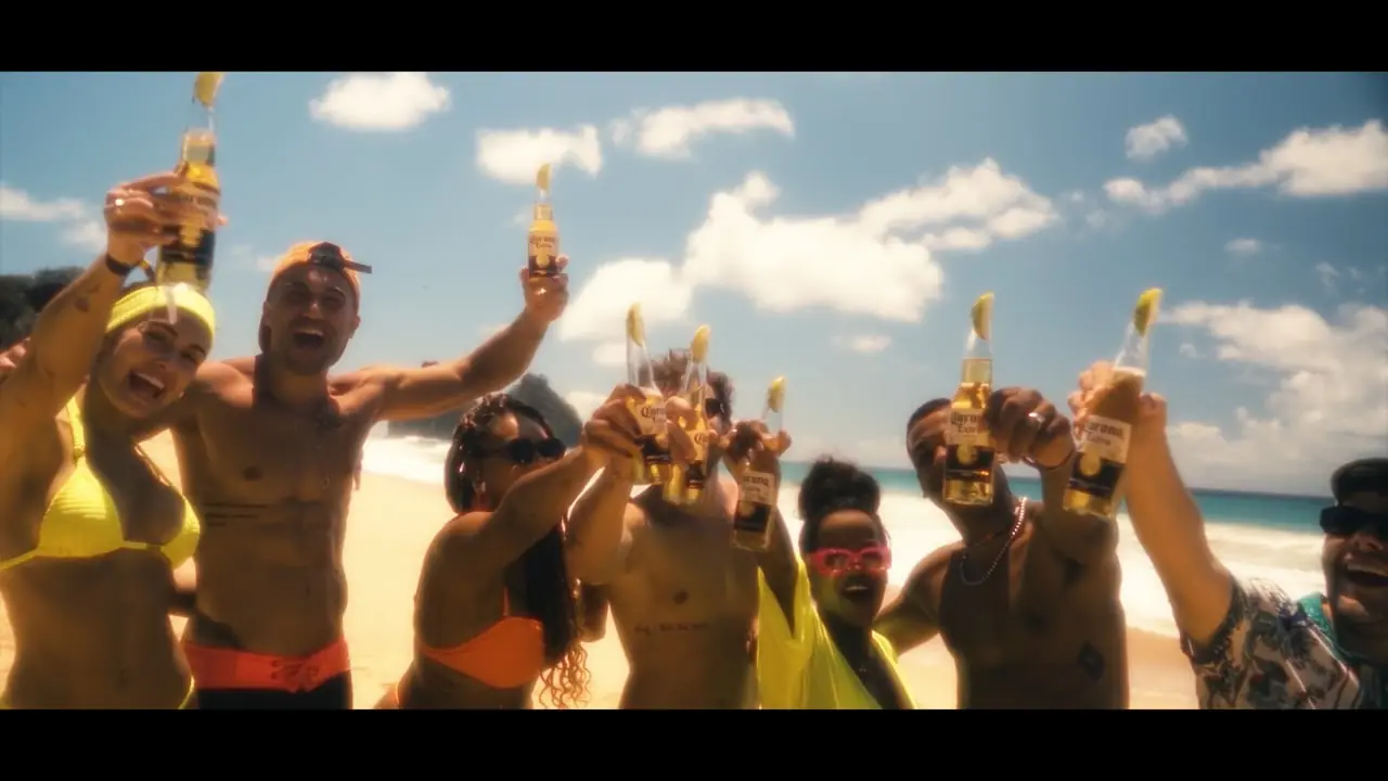 A crowd on a beach raising bottles toward camera in bright sun.